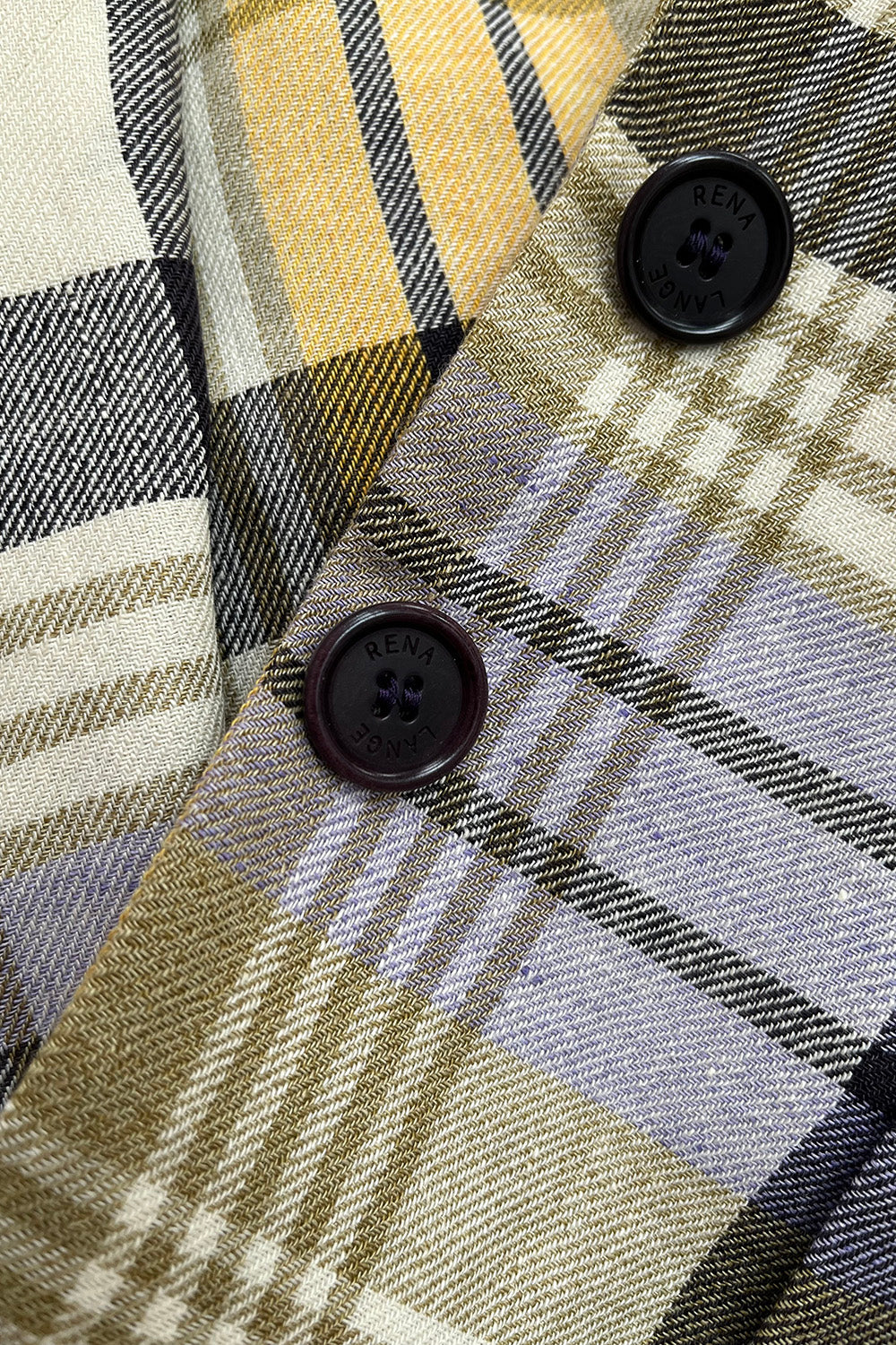 Close-up van twee donkere knopen met Rena Lange merknaam op de geruite vintage blazer.