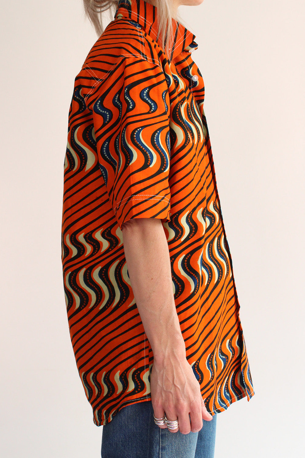 Zijaanzicht authentieke vintage jaren 70 handgemaakt batik shirt in oranje, crème, blauw en zwart, deadstock oversized blouse met grote puntkraag en korte mouwen